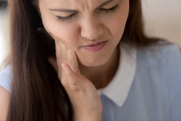 how does tooth decay develop (1) girl holding jaw in pain not knowing How Does Tooth Decay Develop